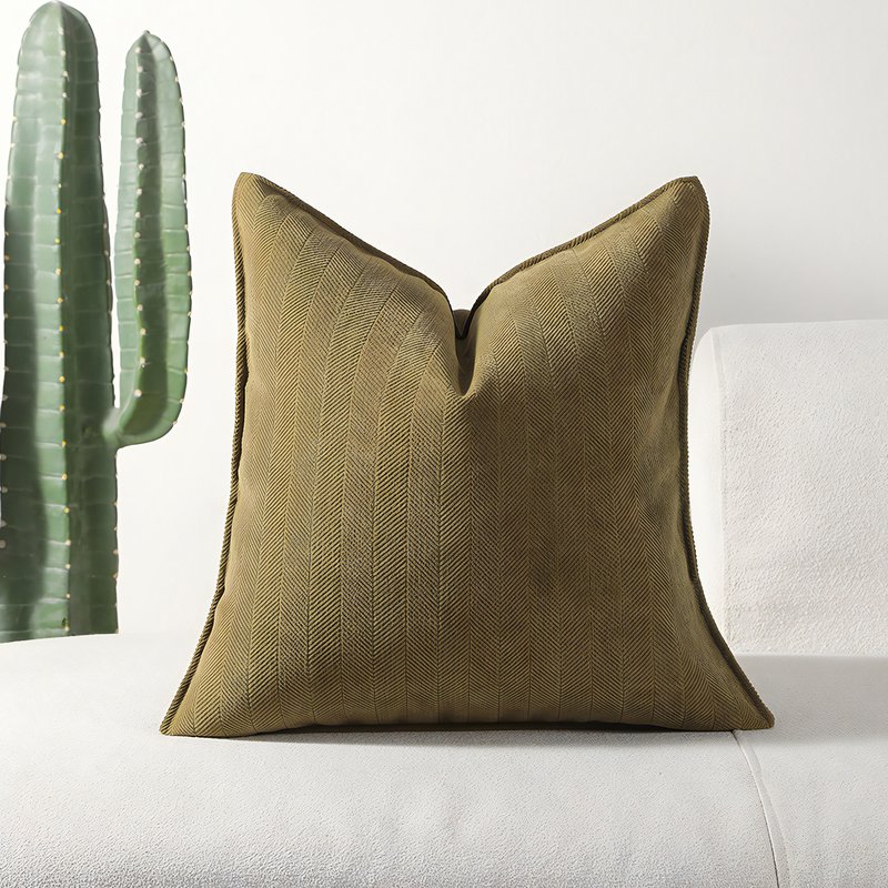 Coussin kaki posé sur un canapé blanc avec un cactus en arrière plan